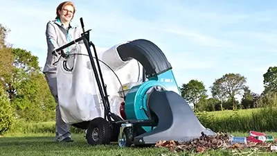 Frau saugt Laub und Abfall von Rasen mit Gerät zur Grundstückspflege