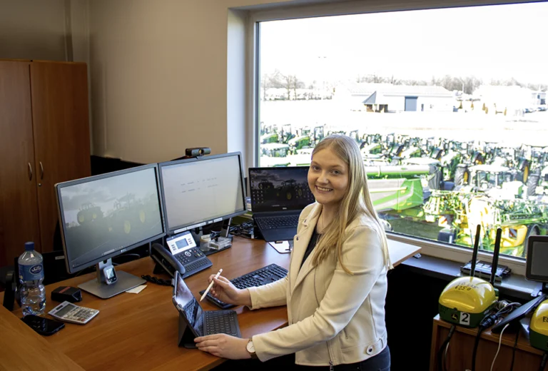 Frau am Schreibtisch lächelt bei der Arbeit in die Kamera