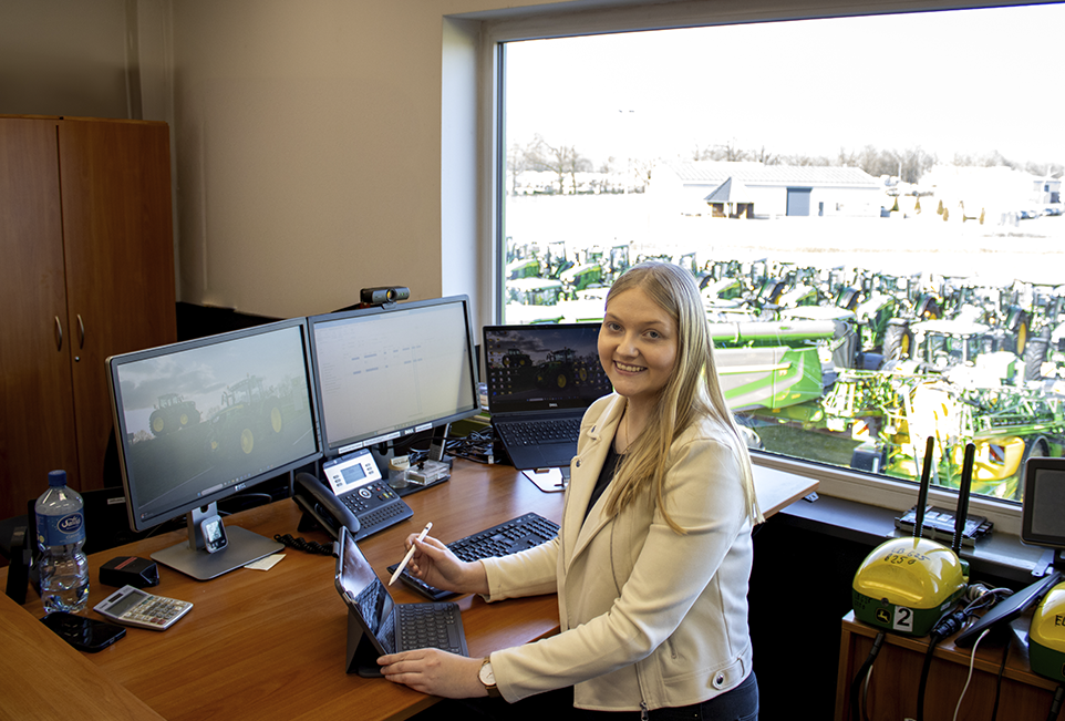 Frau am Schreibtisch lächelt bei der Arbeit in die Kamera